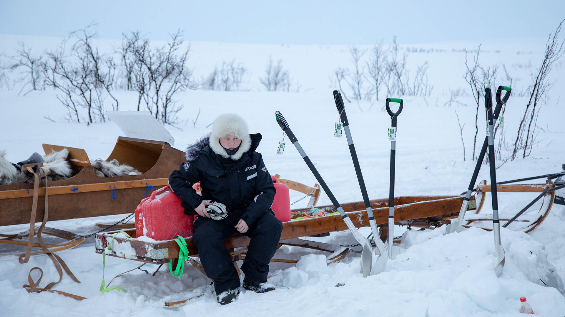 A student in a snowsuit sitting on a sled with gas canisters