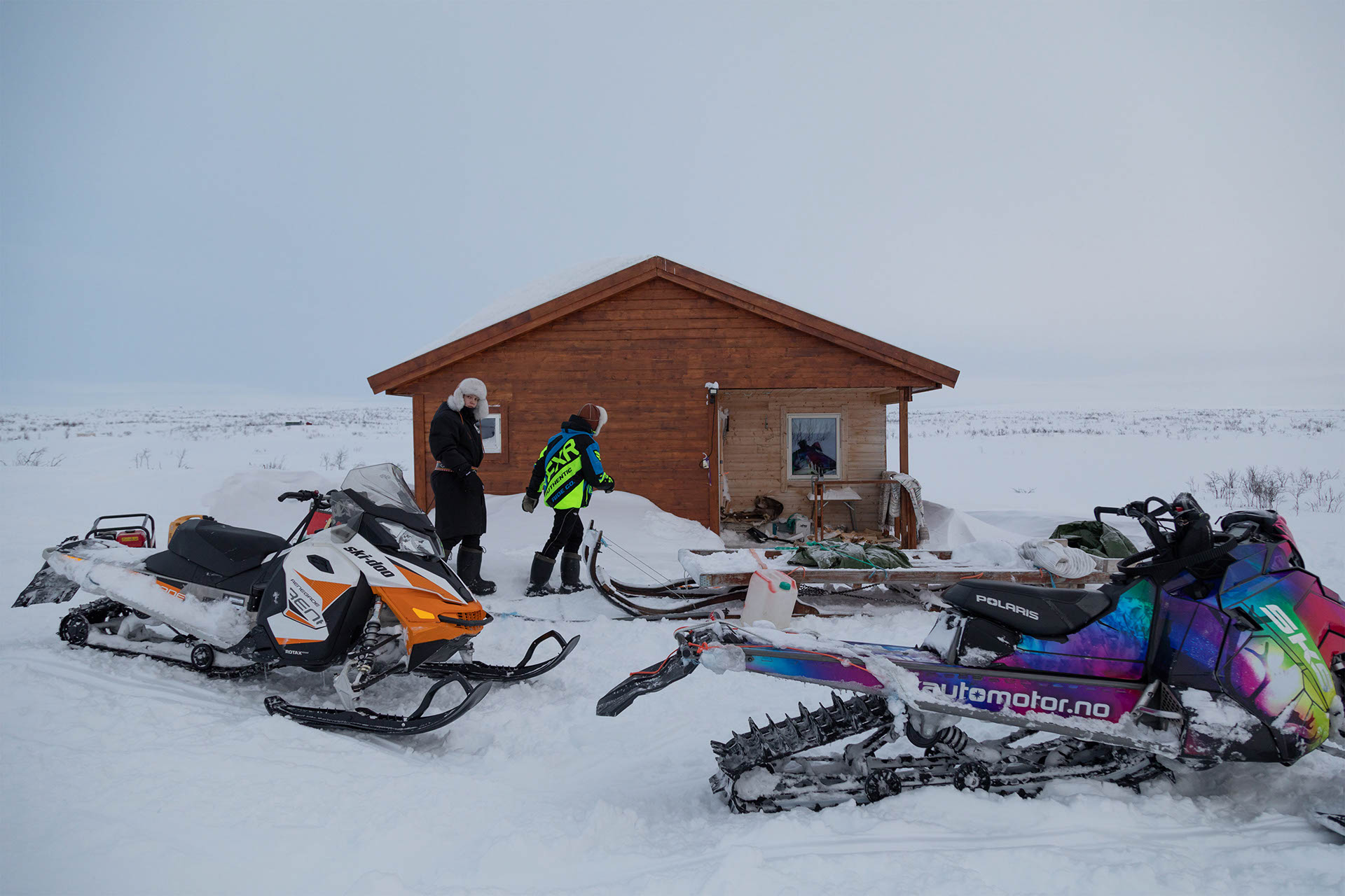 Two students arriving at their cabin with snowmobiles parked out front