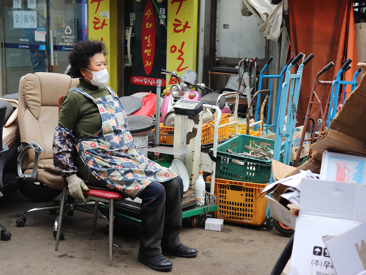 A woman sitting on a red chair outside a recycling depot.