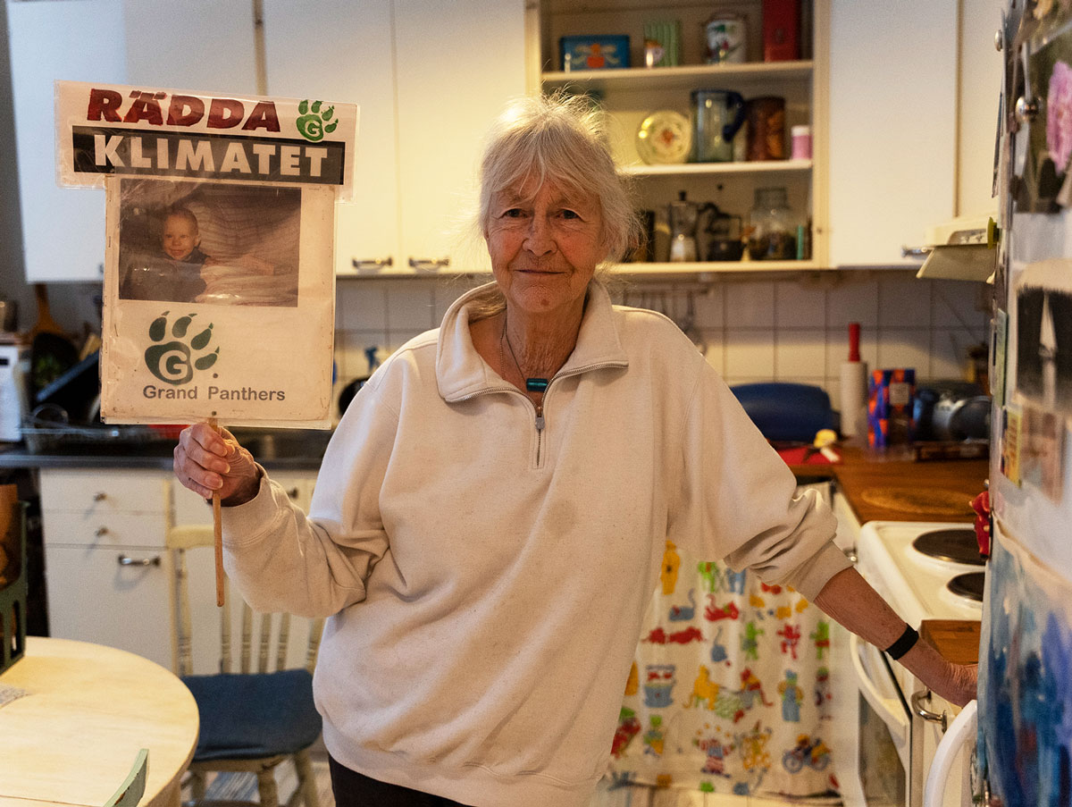 A woman standing in her kitchen holding a Grand Panthers sign.
