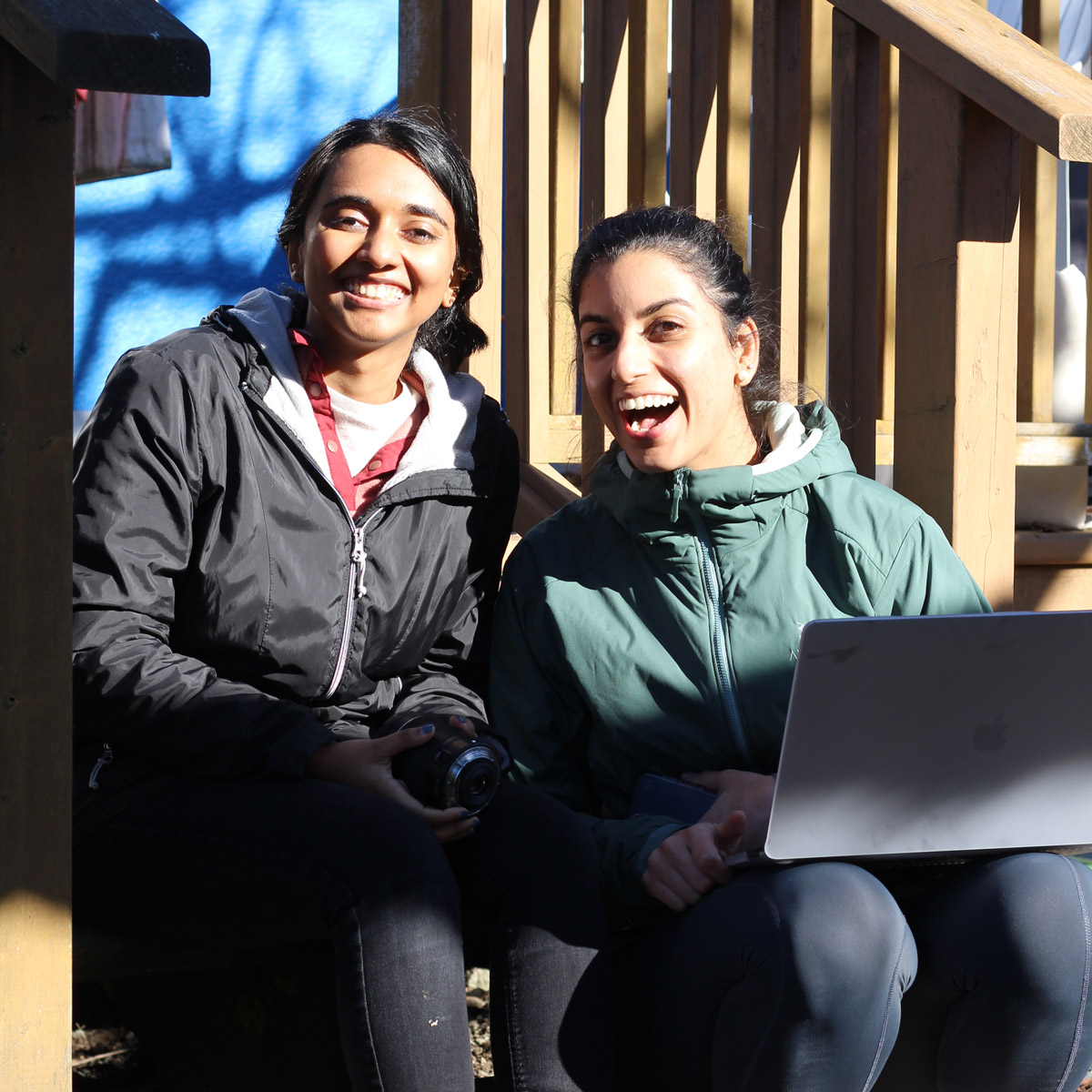Two journalists sitting on porch steps with a laptop